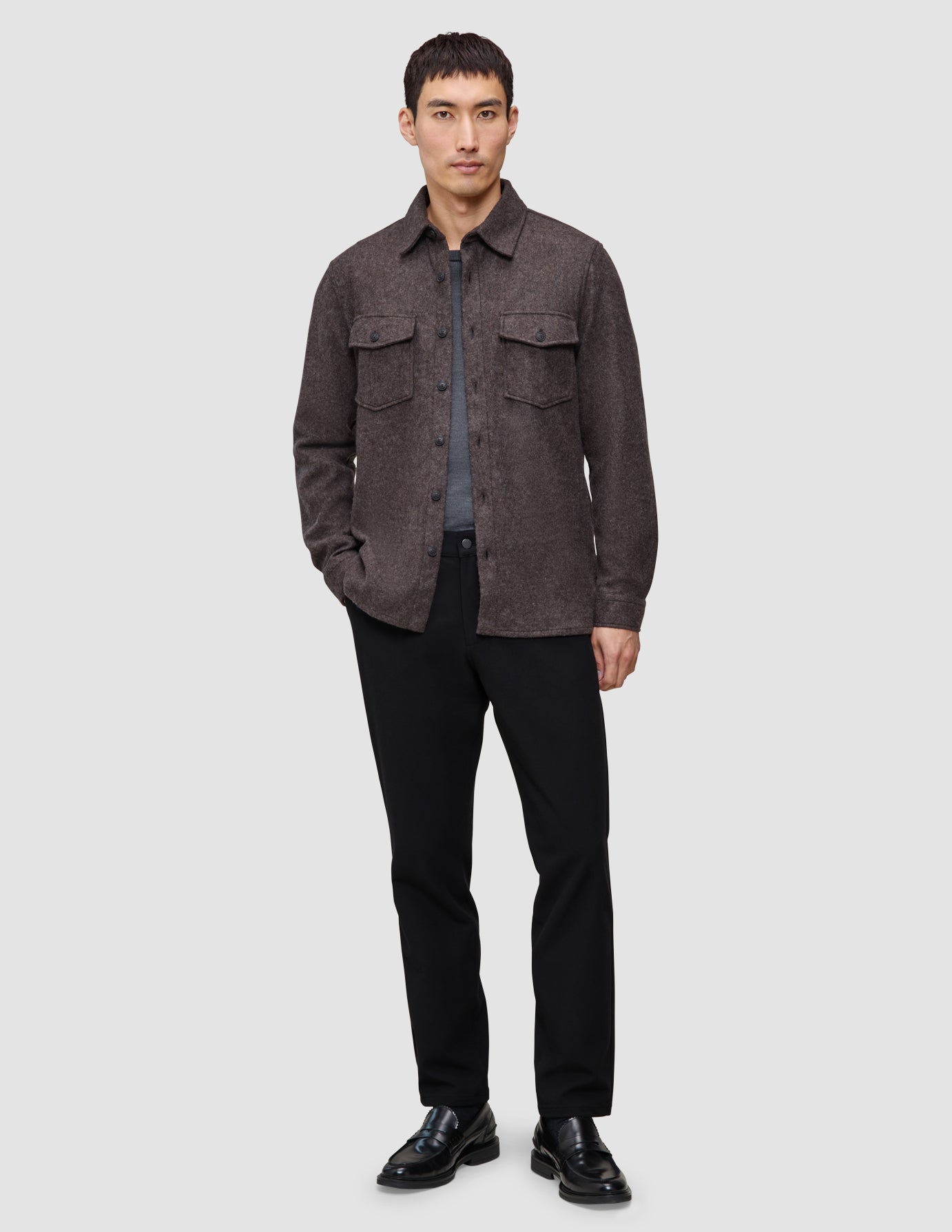 A man wearing a Double Layer Wool Overshirt Saddle Brown over a grey t-shirt, black trousers, and black loafers, reflecting a clean Scandinavian design.